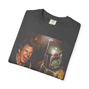 May include: A charcoal gray t-shirt featuring a graphic print of a laughing man with dark hair next to a green and brown armored character wearing a helmet with a T-shaped visor. The shirt has a crew neckline and a visible interior neck label.