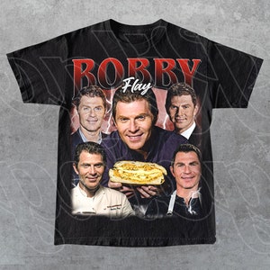 May include: Black t-shirt with a vintage-style graphic featuring a collage of images of chef Bobby Flay. The graphic includes the text "Robby Flay" in red and white letters. The graphic also includes a photo of a sandwich.