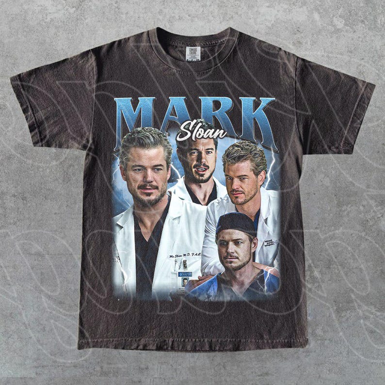 May include: Dark brown t-shirt with a vintage-style graphic of Mark Sloan from Grey's Anatomy. The design includes multiple images of the character with the name "MARK Sloan" in blue text. The shirt has a worn, distressed appearance.