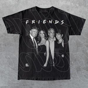 Peut inclure: T-shirt noir avec une image en niveaux de gris de quatre personnes et le mot "FRIENDS" en blanc au-dessus. Le t-shirt est fait d'une mati&egrave;re douce et confortable.