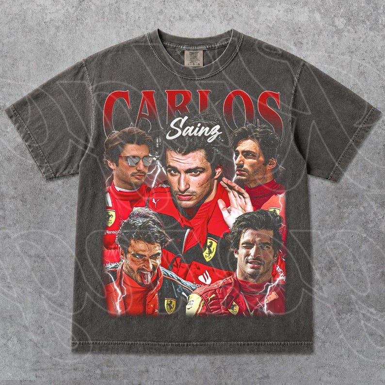 Op de afbeelding: Donkergrijze t-shirt met een vintage-stijl afbeelding van Carlos Sainz in een rood racepak. De tekst "CARLOS Sainz" is in het rood boven de afbeeldingen gedrukt. De t-shirt heeft een ronde hals en korte mouwen.