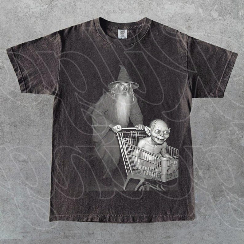 May include: Dark grey t-shirt with a black and white graphic of Gandalf pushing a shopping trolley with Gollum inside. The design is a parody of the Lord of the Rings. The shirt has a vintage, distressed appearance.