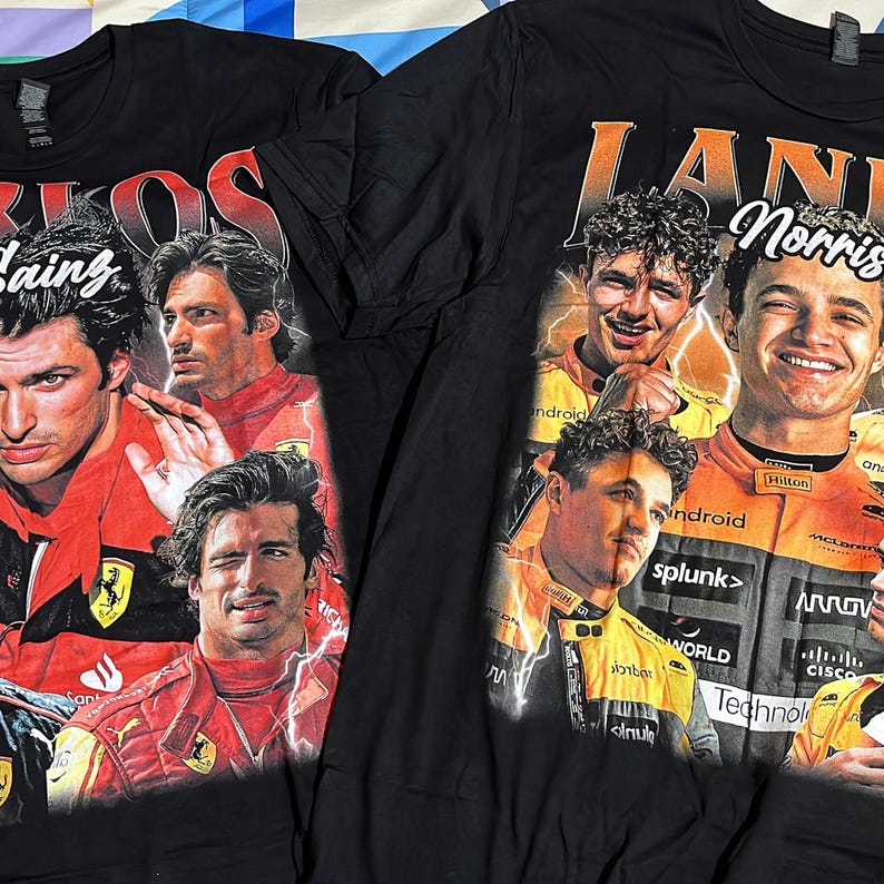 Op de afbeelding: Twee zwarte t-shirts met Formule 1-coureurs. E&eacute;n shirt toont Carlos Sainz met het woord "SAINZ" in rood. Het andere shirt toont Lando Norris met de naam "Norris" en het woord "LANI" in oranje.