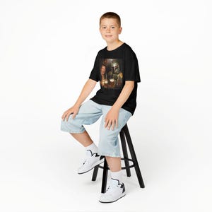 May include: A black short-sleeve t-shirt featuring a graphic print of a person and a character in a helmet holding beer mugs. The shirt is made of a dark fabric and displays a detailed, colorful scene of the two figures clinking their glasses.
