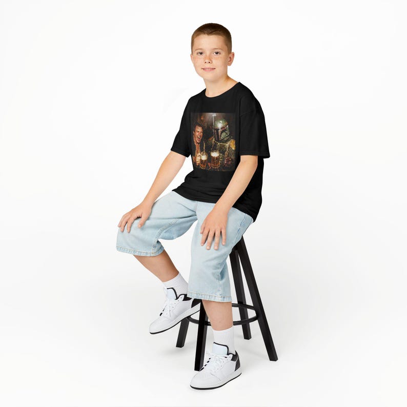 May include: A black short-sleeve t-shirt featuring a graphic print of a person and a character in a helmet holding beer mugs. The shirt is made of a dark fabric and displays a detailed, colorful scene of the two figures clinking their glasses.