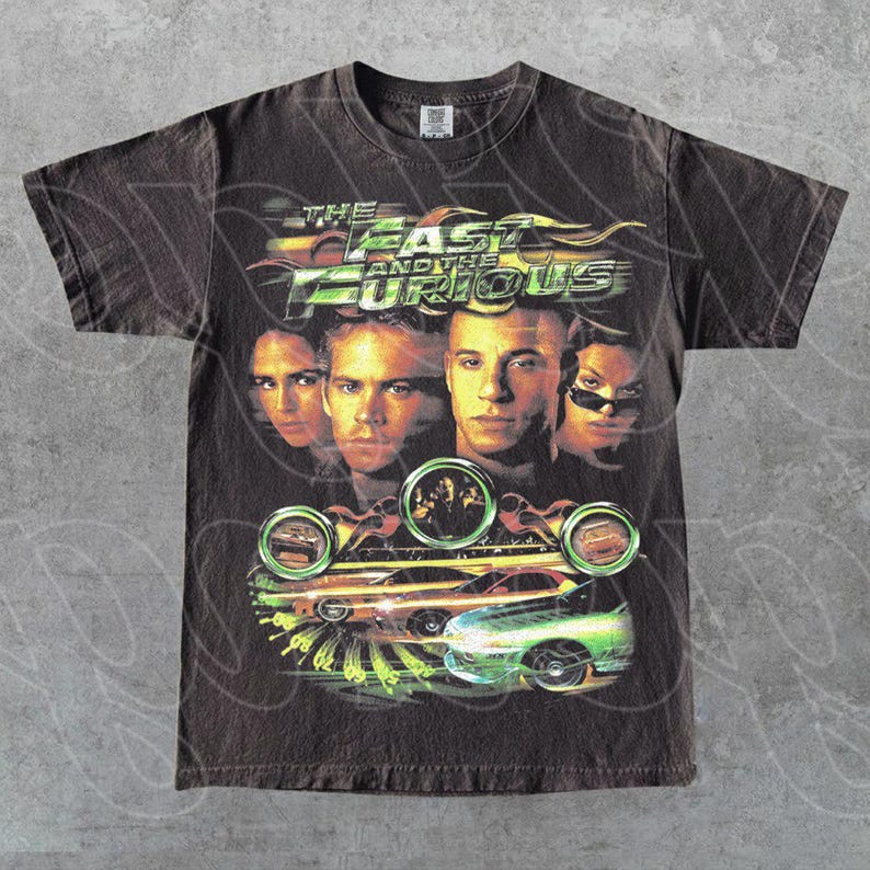 May include: Dark brown t-shirt with the film title "The Fast and the Furious" and images of the actors and cars. The design features the movie title in green and yellow, with images of the actors and cars in the foreground.