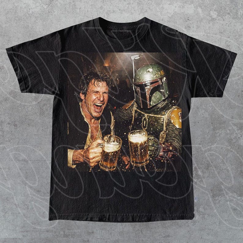 May include: A black short-sleeve t-shirt featuring a graphic print of a laughing man in a vest and a character in a green and brown helmeted suit, both holding glass beer mugs filled with a golden liquid in a dimly lit setting.