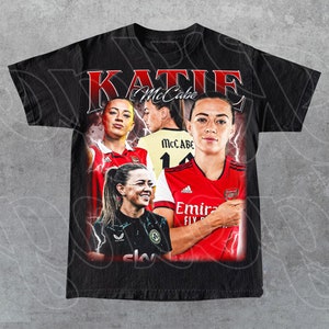 Könnte beinhalten: Schwarzes T-Shirt mit einem Grafikdruck im Vintage-Stil, der Katie McCabe, eine Fußballspielerin, zeigt. Die Grafik enthält ihren Namen "Katie McCabe" und ihre Trikotnummer "11".