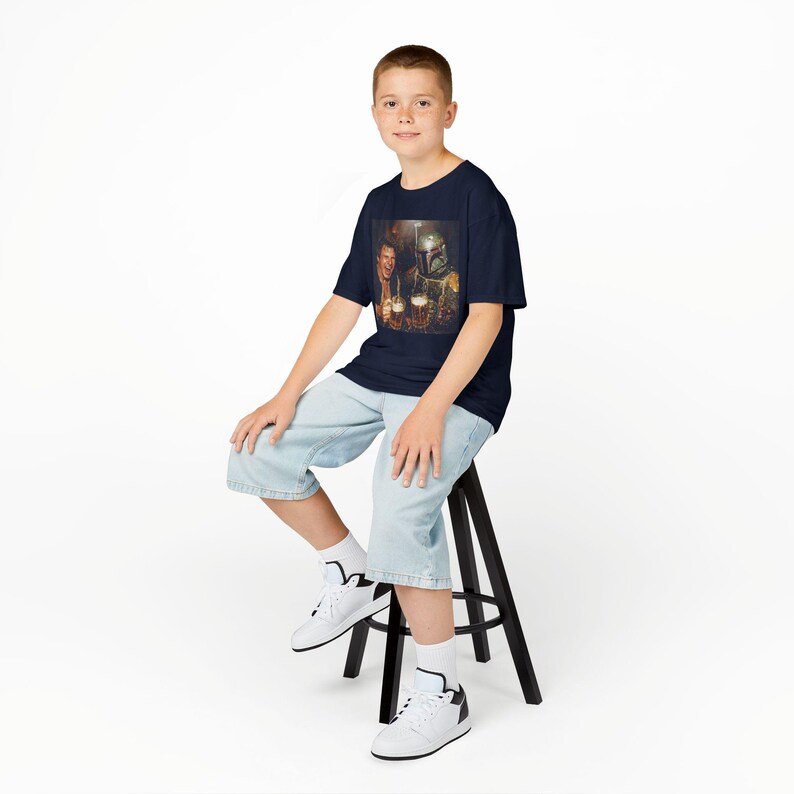 May include: A navy blue short-sleeve t-shirt featuring a graphic print of a human character and a helmeted bounty hunter character holding mugs of beer. The shirt has a crew neckline and a standard fit, showcasing a detailed, colorful illustration.