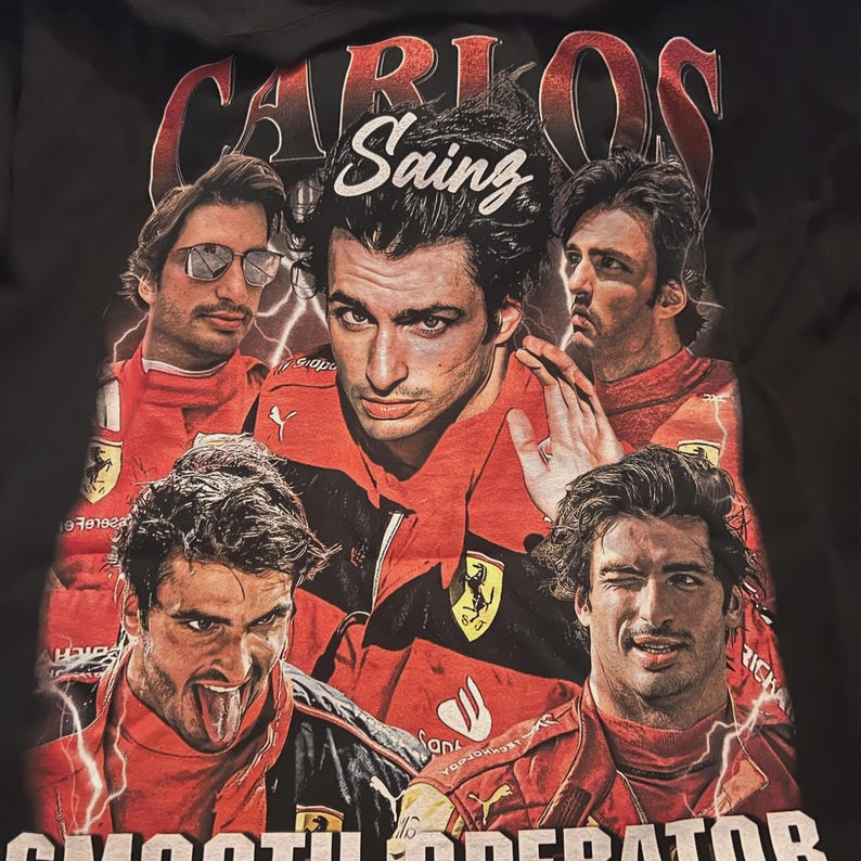 Op de afbeelding: Zwart T-shirt met een collage van afbeeldingen van Carlos Sainz in een rood racepak. De tekst "CARLOS Sainz" staat boven de afbeeldingen en "SMOOTH OPERATOR" staat onderaan. Er zijn ook bliksemflitsen.