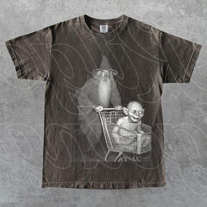 May include: Dark brown t-shirt with a black and white graphic of a wizard pushing a shopping trolley with a creature inside. The design is a parody of a famous fantasy story. The shirt has a crew neck and short sleeves.