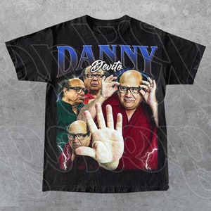 May include: Black t-shirt featuring a collage of Danny DeVito images with the name "DANNY" in blue and "DeVito" in white. The design includes lightning bolt graphics and a vintage aesthetic.