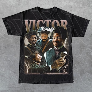 May include: Black t-shirt featuring a vintage-style graphic of a man with glasses and a mustache, with the text "VICTOR Timely" in a retro font. The design includes lightning bolt accents and multiple images of the man.