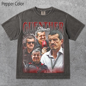 May include: A pepper-colored short-sleeve t-shirt featuring a graphic print of Guenther Steiner. The design includes three portraits of the individual, the text GUENTHER in red, and the name Steiner in white script, set against a dark background.
