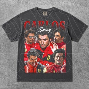 Op de afbeelding: Donkergrijze t-shirt met een vintage-stijl afbeelding van Carlos Sainz in een rood racepak. Het ontwerp bevat meerdere afbeeldingen van Sainz en de tekst "CARLOS Sainz" in het rood. Het t-shirt heeft een versleten uitstraling.