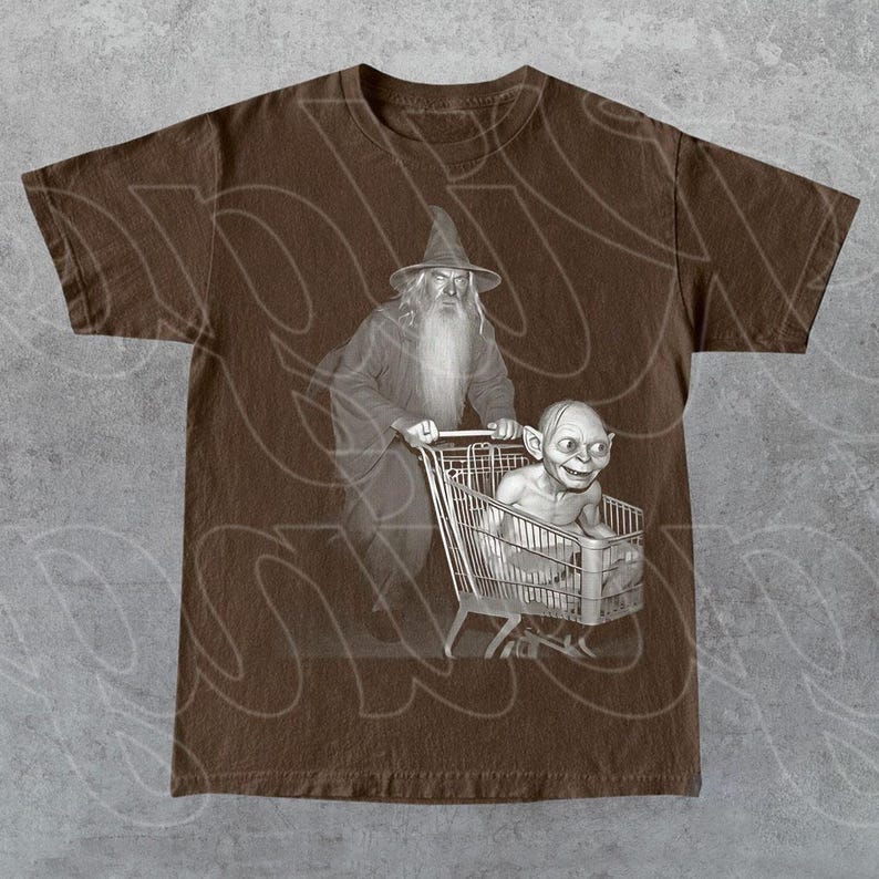May include: Brown t-shirt with a sepia-toned graphic of a wizard pushing a shopping trolley with a creature inside. The wizard wears a tall hat and long beard. The creature is in the trolley, smiling. The shirt has a crew neck.