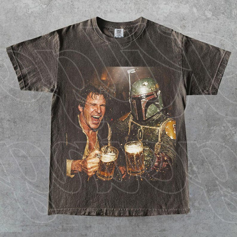 May include: A charcoal gray short-sleeve t-shirt featuring a graphic print of a smiling man and a character in a green and yellow helmet holding glass beer mugs. The shirt has a crew neckline and a distressed, vintage-style wash throughout the fabric.