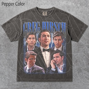 May include: Pepper color t-shirt featuring a graphic of Greg Hirsch in various poses, with the name "GREG HIRSCH" in blue text. The shirt has a vintage, distressed look.