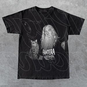 May include: Black t-shirt featuring a grayscale image of a man with a long white beard and a cat. The word "PANTERA" is printed in white on the shirt. The shirt is a crew neck style.