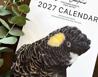 May include: A 2027 wall calendar featuring a detailed coloured pencil illustration of a black cockatoo with a yellow ear patch. The cover text reads Jenna Chartrand Coloured Pencil Fine Artist 2027 Calendar featuring twelve original artworks.