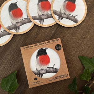 May include: A set of four round wooden coasters featuring a coloured pencil illustration of a robin bird perched on a branch. The coasters are packaged in a square brown cardboard box labelled NATURAL WOODEN COASTER SET and SET OF FOUR.