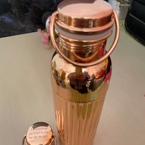 May include: A rose gold water bottle with a matching lid and a handle. The lid has an engraved message that reads "I surrendered my heart to you the day we met."