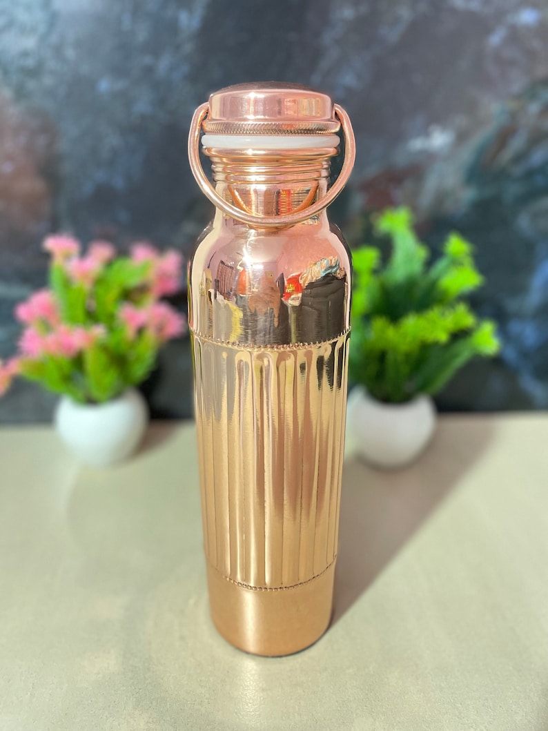 May include: A copper water bottle with a ribbed design and a copper lid with a white seal. The bottle has a handle on the lid.