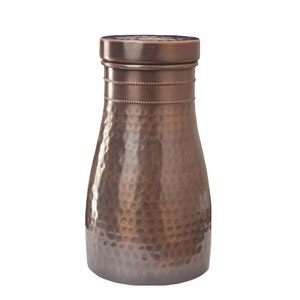 Puede incluir: Una botella de agua de color cobre con una textura martillada. La botella tiene forma cil&iacute;ndrica con una base ligeramente m&aacute;s ancha y un cuello m&aacute;s estrecho. La tapa es plana y la botella mide unos 23 cm de alto.