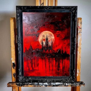 Può includere: Un dipinto incorniciato in nero che raffigura un castello scuro in silhouette contro un cielo rosso con una grande luna piena. Il dipinto ha un'estetica oscura e gotica.