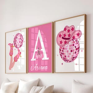 May include: Three framed art prints with a pink theme. One features a disco ball and pink boots, another a large letter "A" with the name "Ariana", and the third a disco ball with a cowboy hat.