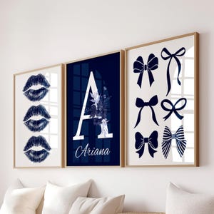May include: Three framed prints with a white background. One print features three dark blue lip prints. Another has a large white letter "A" with floral accents and the name "Ariana". The third print displays various dark blue bow designs.
