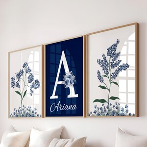 May include: Three framed floral art prints. The prints feature blue floral designs and a navy blue print with the letter "A" and the name "Ariana". The frames are a light brown color.