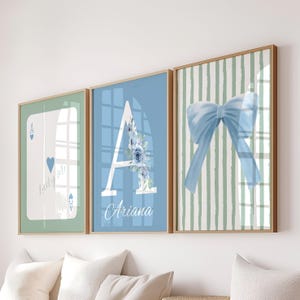 Op de afbeelding: Drie ingelijste wandkunstwerken. De eerste toont een harten aas met de tekst "Lucky Me". De tweede toont een blauwe achtergrond met de letter "A" en de naam "Ariana". De derde toont een blauwe strik op een gestreepte achtergrond.