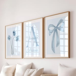 May include: Three framed art prints with watercolor designs. The prints feature a blue floral arrangement, the letter "A" with a bow, and a blue bow. The frames are a light brown color.