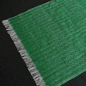 May include: A green fabric table runner with a white fringe border. The runner has a textured woven pattern.