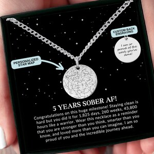 May include: A silver necklace with a round pendant featuring a constellation star map. The necklace comes in a black box with a message that reads "5 Years Sober AF!" and includes a personalized star map and a custom back engraving option.