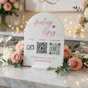 May include: A white arched sign with pink text reading feeling tipsy and please show love to our bartender. It features icons for cash, Venmo, and Cash App with two QR codes. The sign is displayed on a white base with pink roses and greenery.