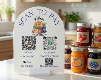 May include: A white arched sign with the text SCAN TO PAY, featuring a logo for Williams Sugar Spreads, three QR codes for Venmo, CashApp, and social media, plus Apple Pay and a phone number. Four glass jars of fruit preserves sit beside the sign.