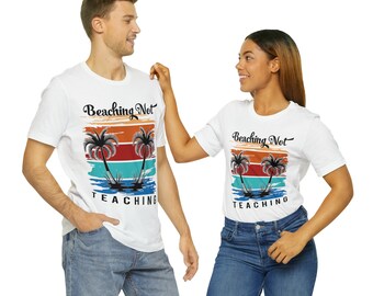 May include: White t-shirts with a graphic design featuring palm trees, a sunset, and the text "Beaching Not Teaching." The design includes orange, red, blue, and black colors. The shirts are worn by two people.