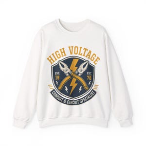 May include: A white long-sleeve sweatshirt featuring a graphic of crossed pliers over a yellow lightning bolt inside a dark blue shield. The text reads HIGH VOLTAGE, EST. 1978, and CONDUIT & CIRCUIT SPECIALIST in yellow and white lettering.
