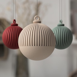 Könnte beinhalten: Drei hängende Zierkugeln in Rot, Creme und Grün. Jede Kugel hat vertikale Rillen und einen strukturierten Boden. Die Kugeln sind an dünnen Schnüren aufgehängt. Ideal für Dekorationen.