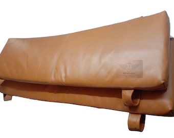 May include: Two brown leather cushions with straps. The cushions are folded in half and the straps are visible on the sides.