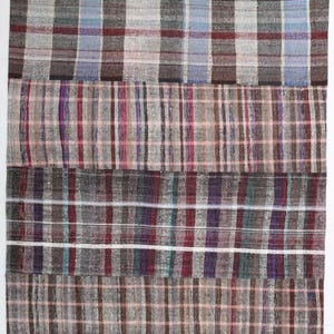 May include: A rectangular area rug featuring a patchwork design composed of four horizontal sections. Each section displays a distinct plaid pattern in varying shades of gray, brown, red, purple, blue, and white, creating a multi-colored textile.