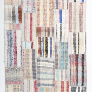 May include: A rectangular area rug featuring a patchwork design composed of various woven fabric strips. The rug displays a multitude of vertical striped patterns in diverse colors including blue, red, yellow, black, white, and grey, stitched together.
