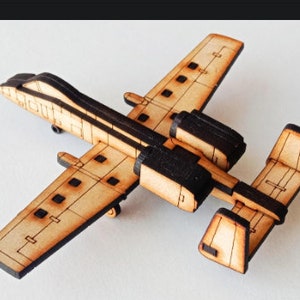 以下が含まれることがあります： 黒いディテールが施された、A-10サンダーボルトII航空機（ウォーホッグとしても知られる）の木製モデル。このモデルはレーザーカットされた木材でできており、組み立てられています。