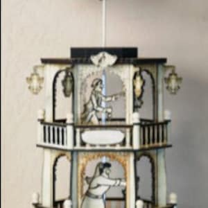 Puede incluir: Un carrusel de madera blanco de tres niveles con una hélice giratoria en la parte superior. El carrusel presenta dos figuras en cada nivel, con un diseño en blanco y negro. El nivel inferior tiene tres velas blancas.