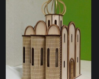 May include: A wooden model of a church with a gold-colored dome and cross. The model has intricate details, including windows and a door. The church is sitting on a white surface.