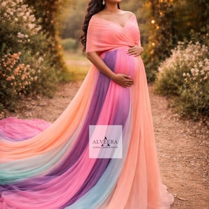 May include: A flowing, off-the-shoulder maternity gown in a rainbow of colors, including peach, purple, and blue. The dress features a long train and the text "ALVEERA ALEENA FASHION HOUSE". The gown is worn outdoors.