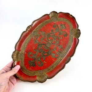 May include: An oval-shaped serving tray with a red base and gold-colored decorative details. The tray has a scalloped edge and a floral design.
