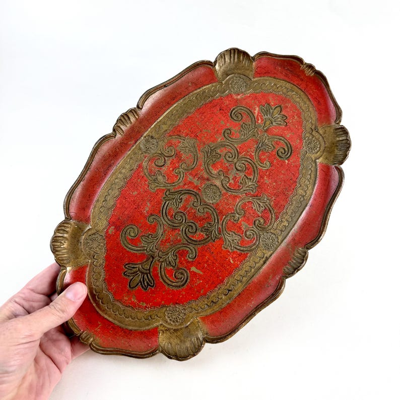 May include: An oval-shaped serving tray with a red base and gold-colored decorative details. The tray has a scalloped edge and a floral design.